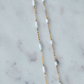 Gold chain necklace with white beads on a marble surface