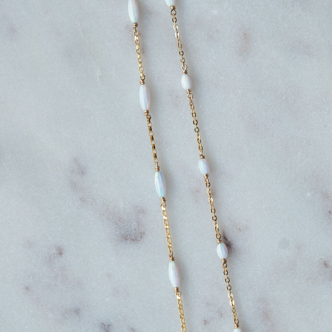 Gold chain necklace with white beads on a marble surface
