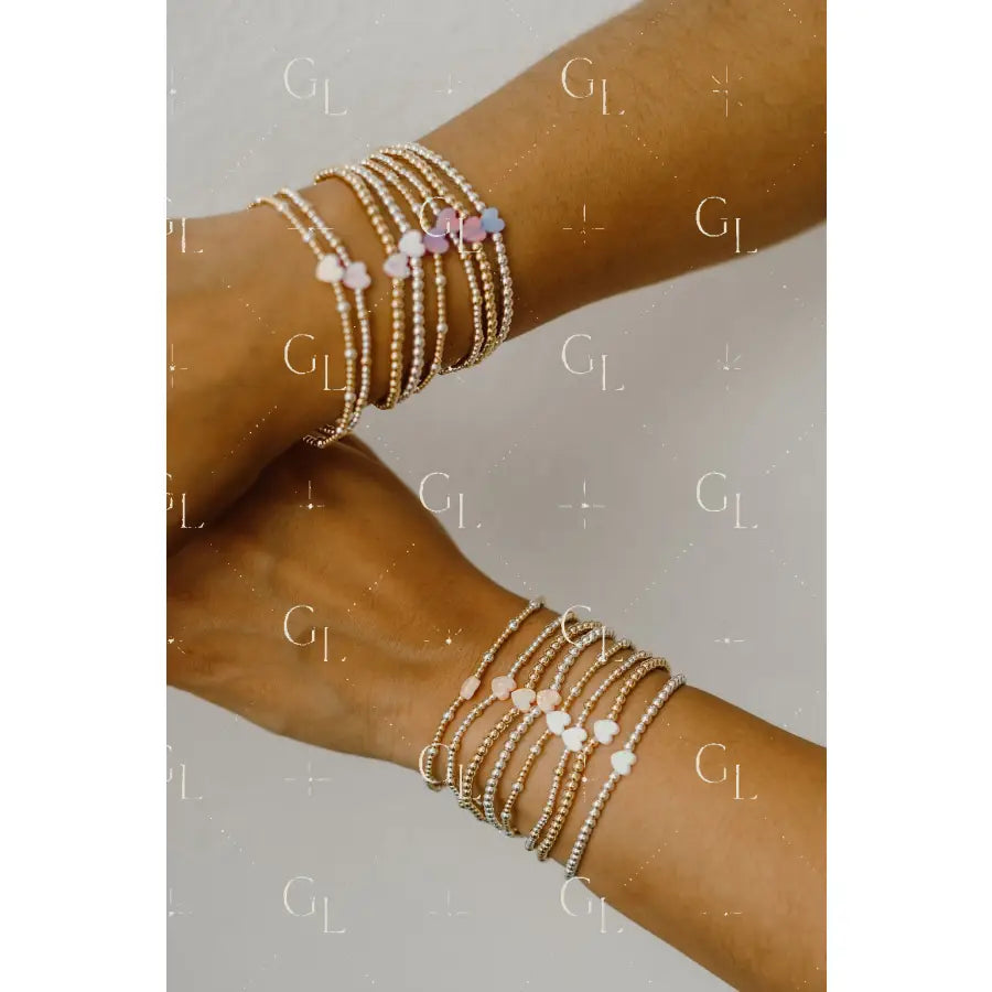 Two arms wearing multiple beaded bracelets on a neutral background