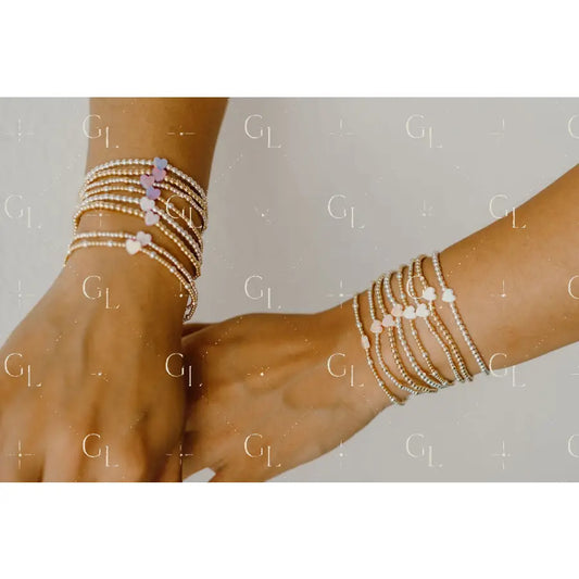 Two hands wearing multiple pearl bracelets on a neutral background