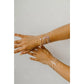 Two hands wearing multiple gold bracelets on a light gray background