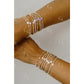 Two arms wearing multiple beaded bracelets on a neutral background