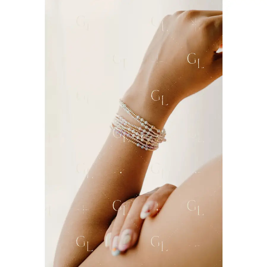 Hand wearing multiple pearl bracelets on a light background