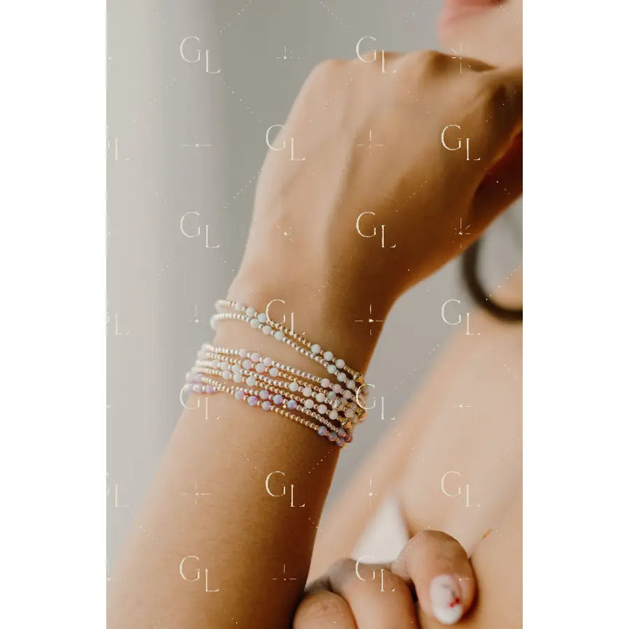 Close-up of a wrist wearing multiple pearl bracelets on a neutral background