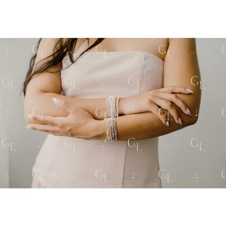Woman wearing multiple pearl bracelets on her wrist with a neutral background