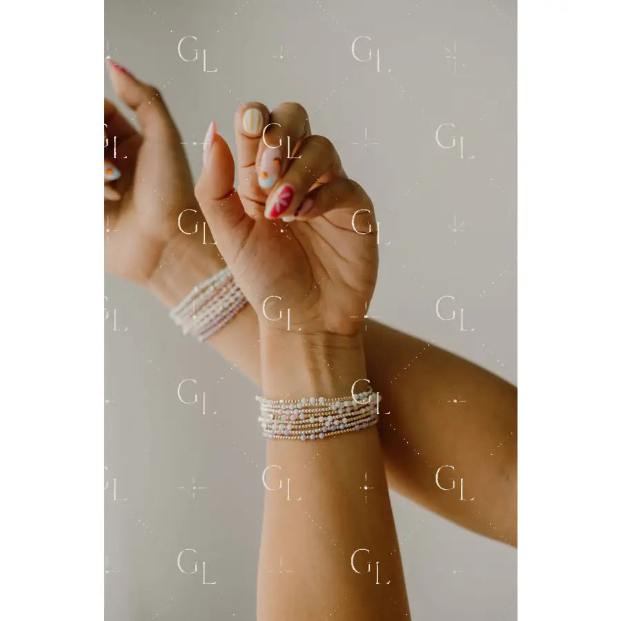 Close-up of a wrist with multiple pearl bracelets on a neutral background