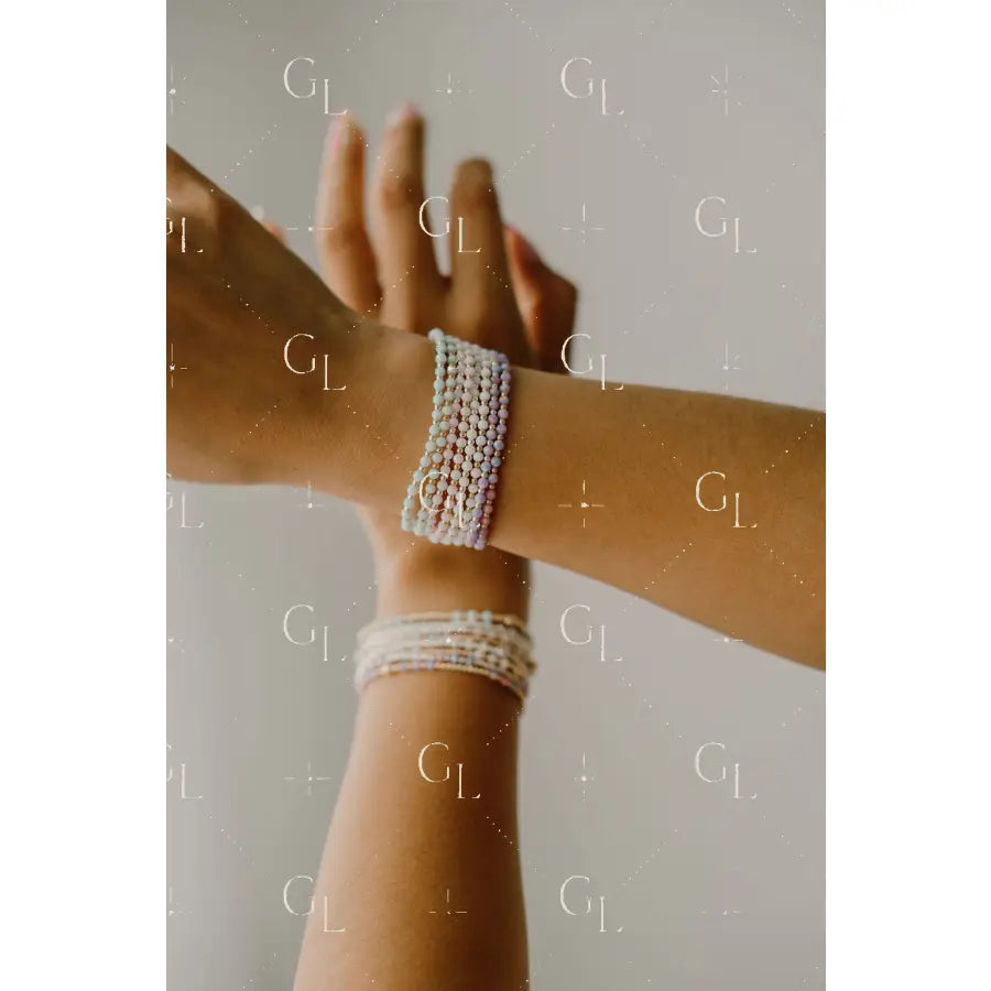 Two arms with pearl bracelets on a neutral background