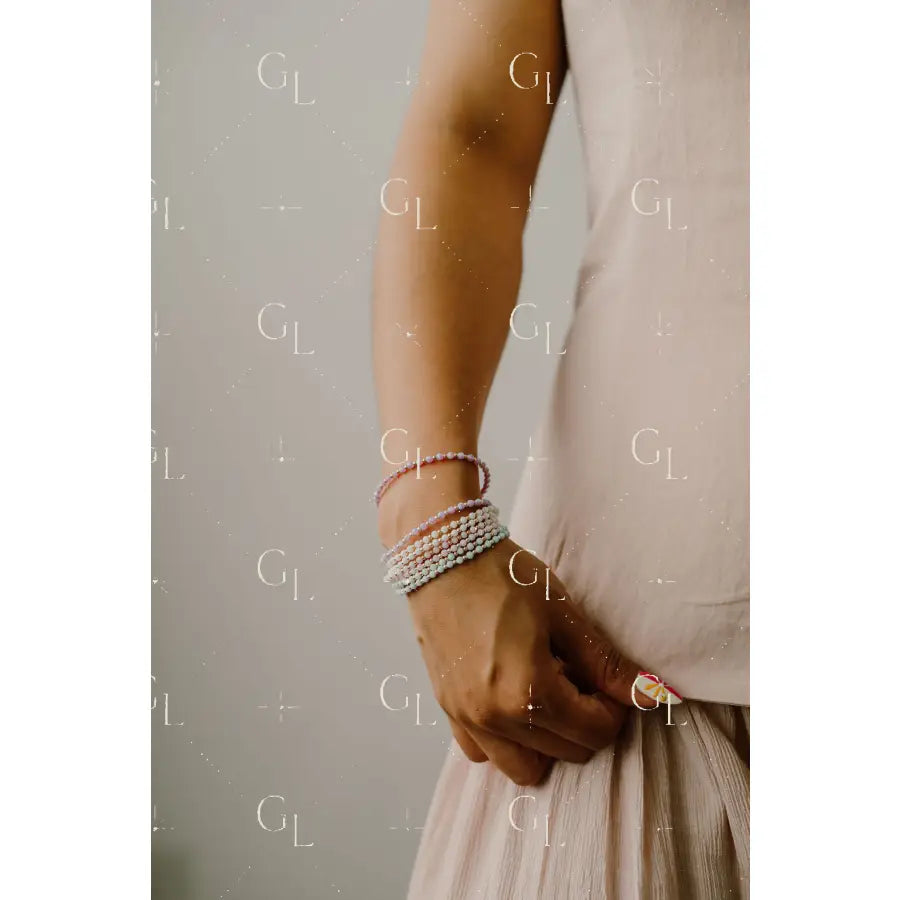 Person wearing multiple opal bracelets on a neutral background