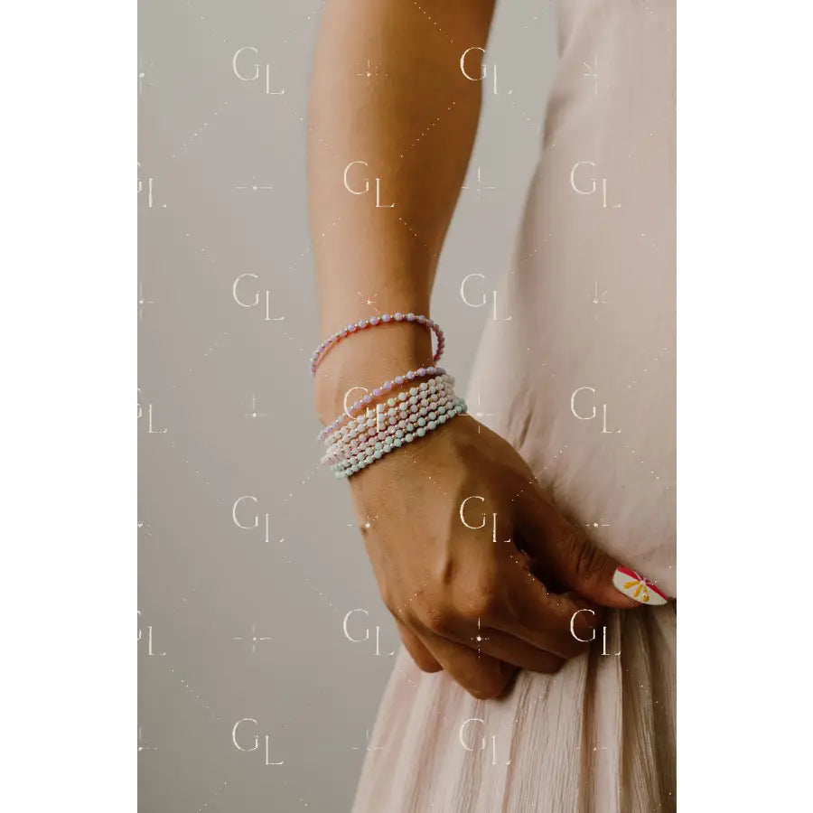 Close-up of a person's wrist wearing multiple pearl bracelets on a neutral background