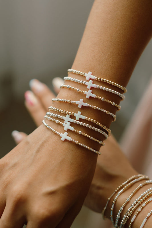 Close-up of a wrist wearing multiple delicate bracelet with cross designs.