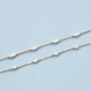 Gold chain with white beads on a light blue background
