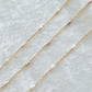 Two gold necklaces with pink pearls on a light gray background