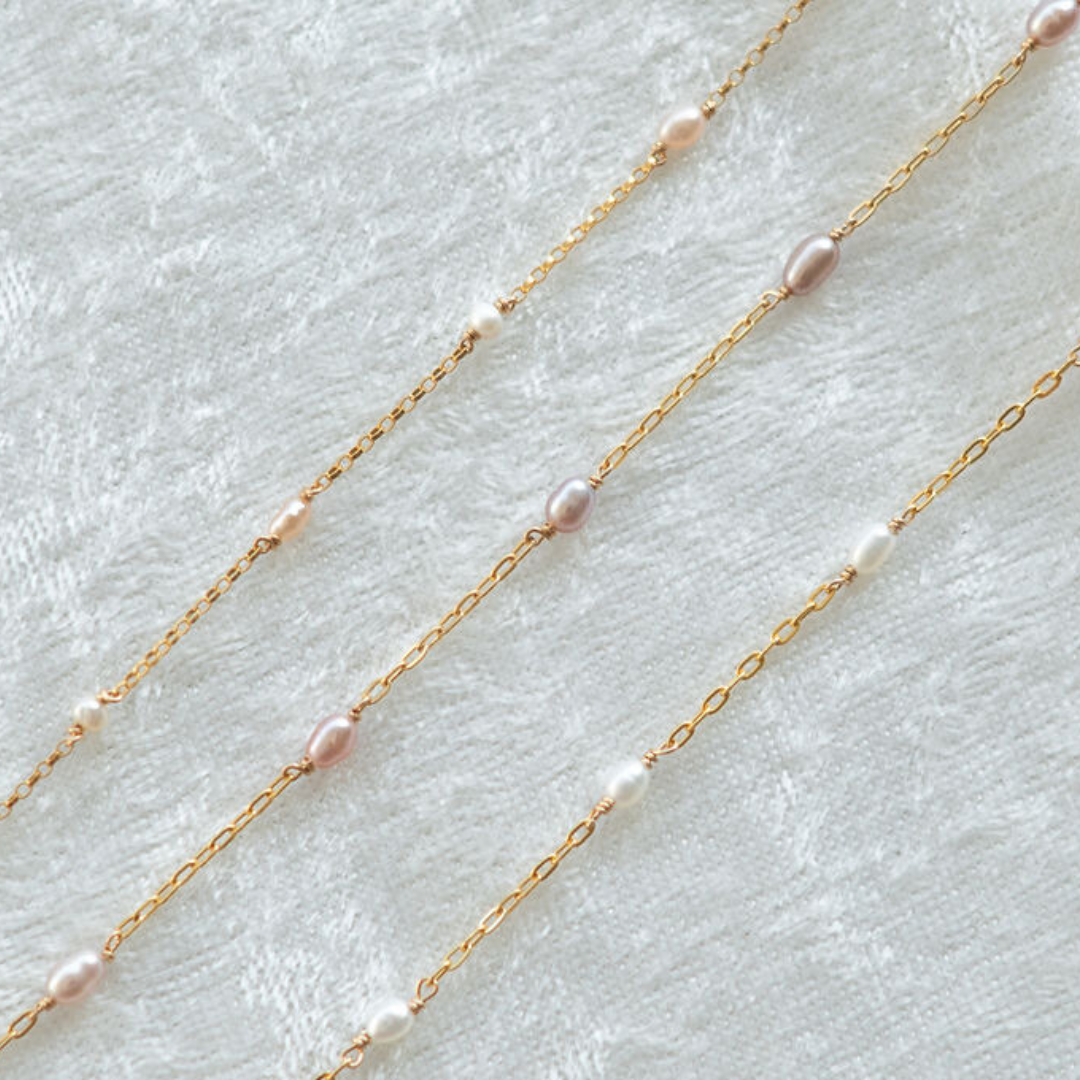 Two gold necklaces with pink pearls on a light gray background