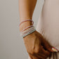 Close-up of a person's wrist wearing multiple pearl bracelets on a neutral background