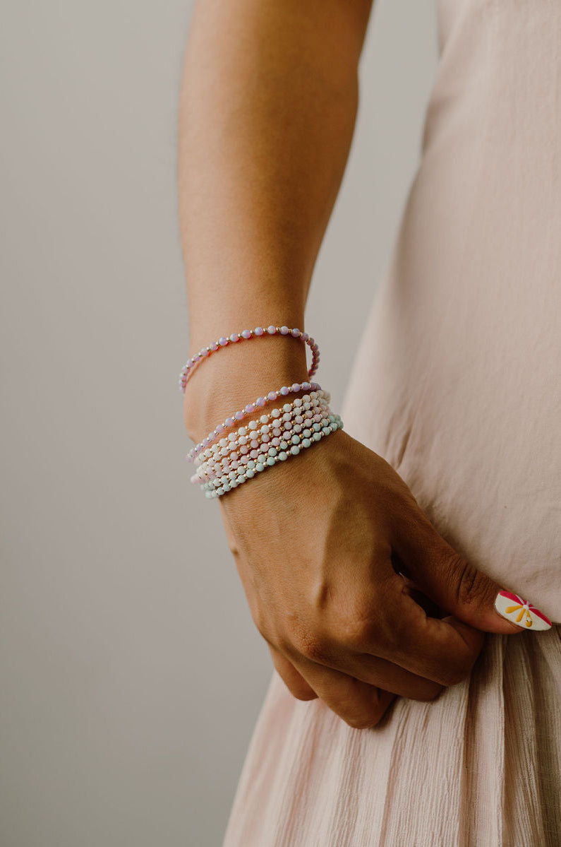 Close-up of a person's wrist wearing multiple pearl bracelets on a neutral background
