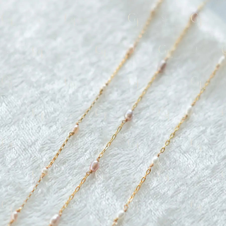 Gold chain necklace with small pearls on a white fabric background