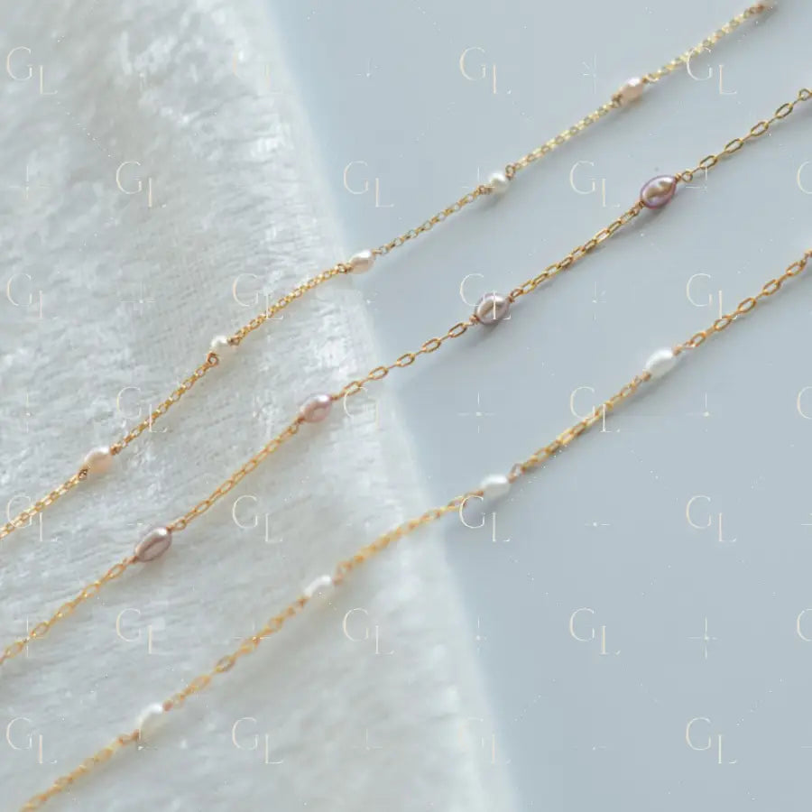 Two gold necklaces with small pearls on a light gray background