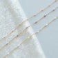 Three delicate gold necklaces with small beads on a textured white surface.