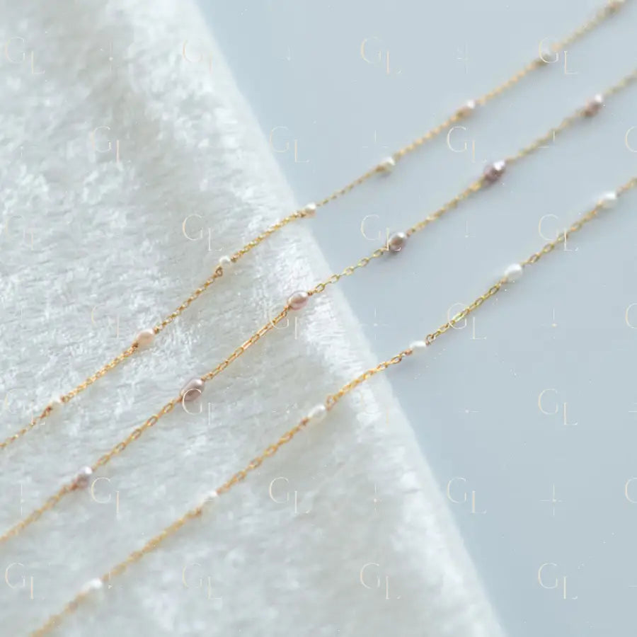 Three delicate gold necklaces with small beads on a textured white surface.