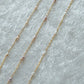 Gold chain necklace with pink pearls on a light gray background