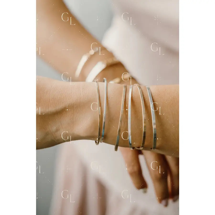 Close-up of a wrist wearing multiple gold bracelets on a neutral background