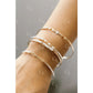 Close-up of a wrist wearing multiple gold Permanent Jewelry Bangle bracelets on a neutral background