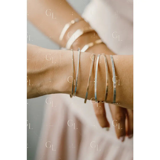 Close-up of a wrist wearing multiple silver bracelets on a neutral background Permanent Jewelry Bangle 