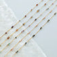 Gold chain necklaces with small beads on a white fabric background
