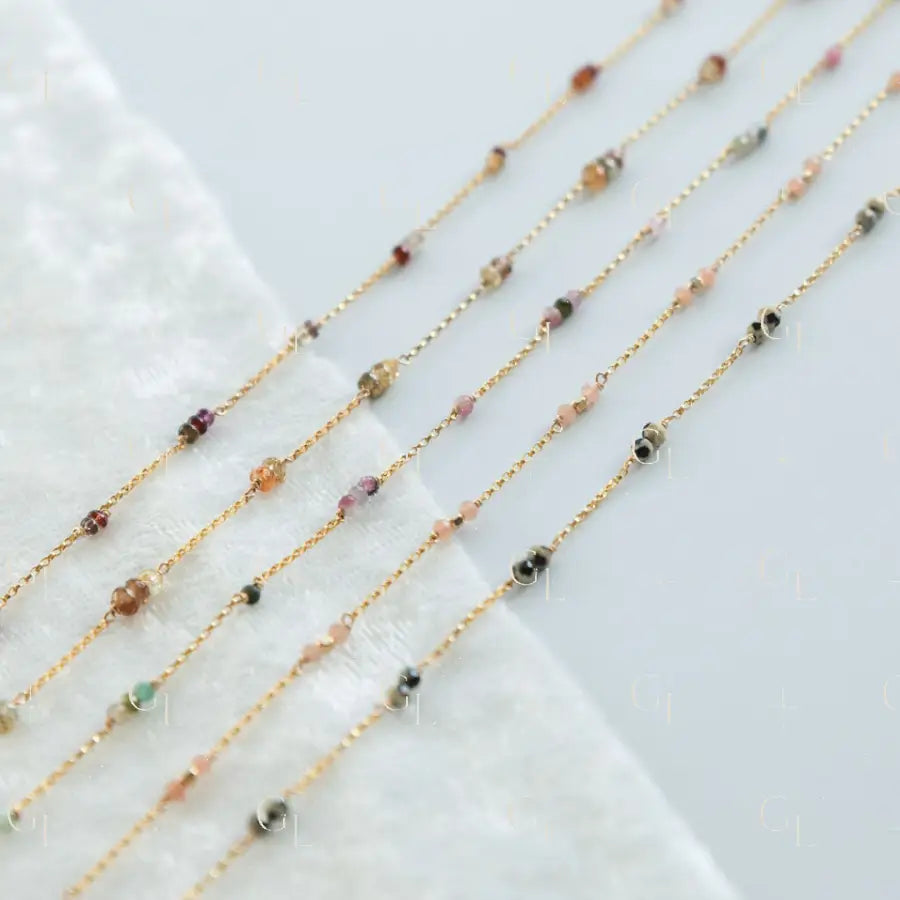 Gold chain necklaces with small beads on a white fabric background