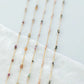 Delicate gold necklaces with small beads on a white fabric background