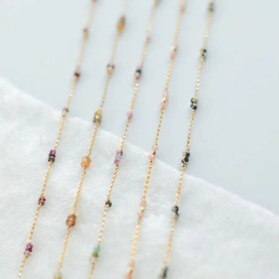 Delicate gold necklaces with small beads on a white fabric background