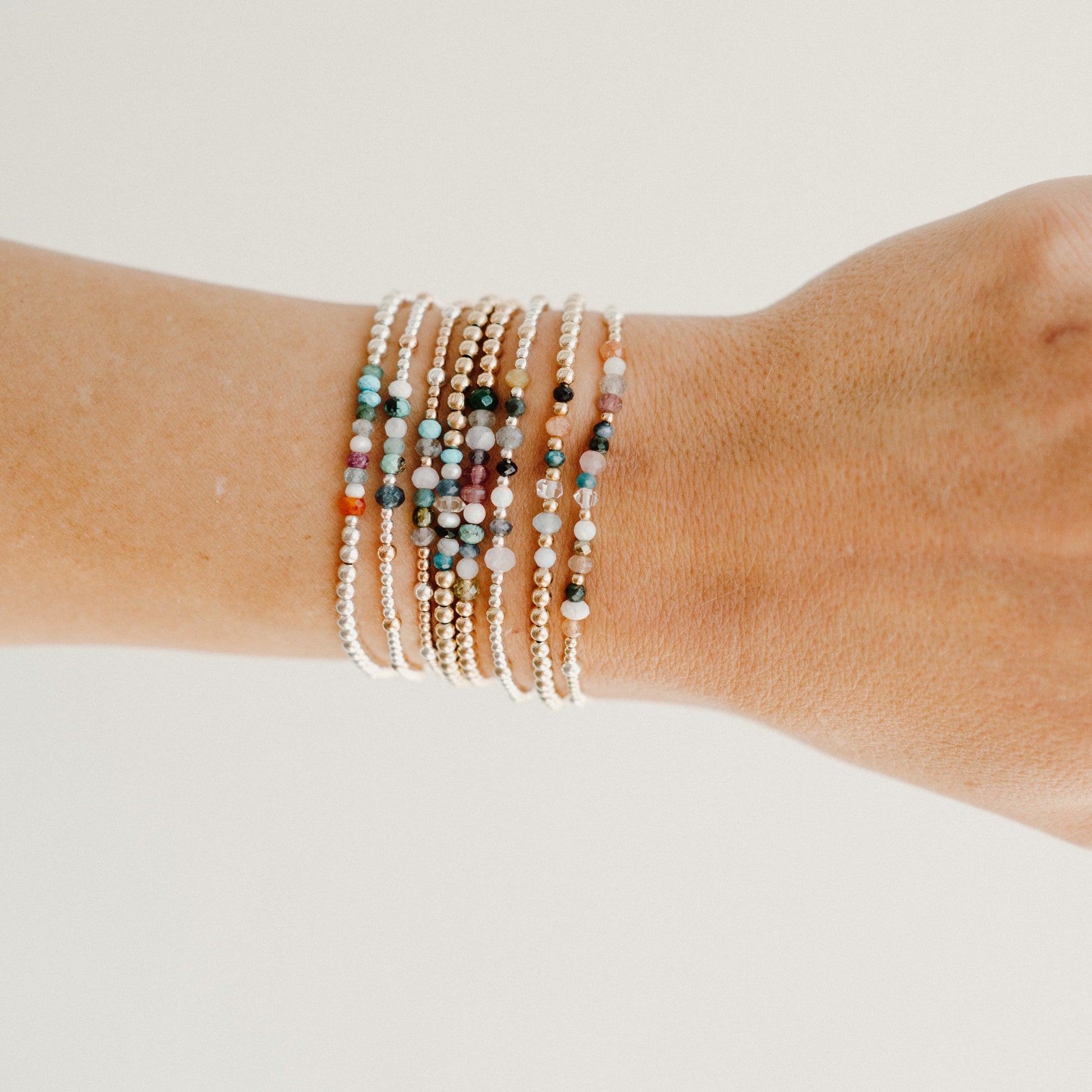Multiple beaded bracelets on a wrist against a neutral background