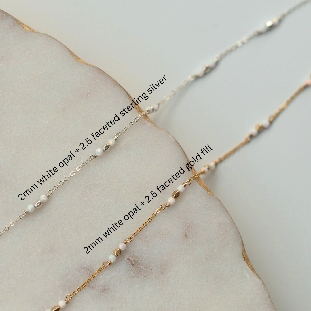 Two gold necklaces with white opal beads on a marble surface