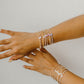 Two hands wearing multiple gold bracelets on a light gray background