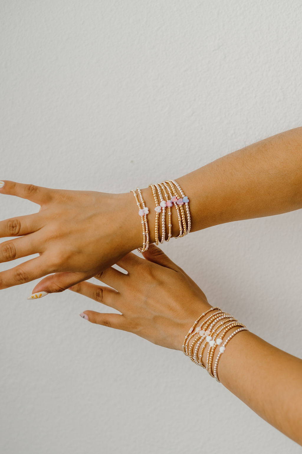 Two hands wearing multiple gold bracelets on a light gray background