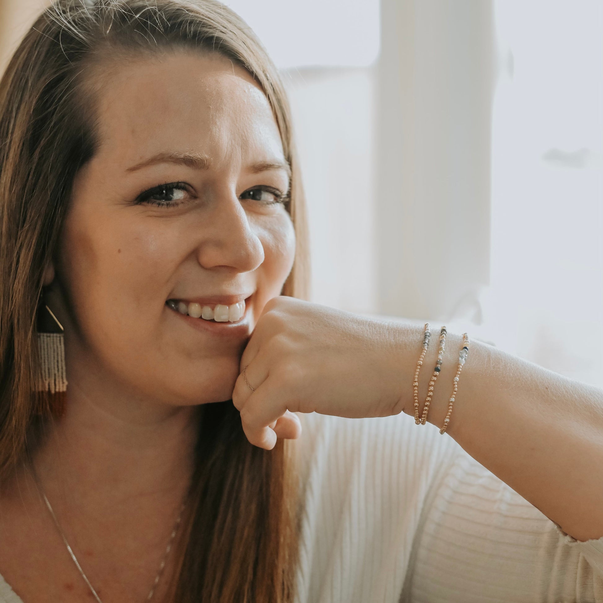 Woman smiling with hand on chin, wearing earrings and bracelets.