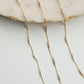 Gold chain necklace with small beads on a light gray surface