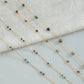 Gold chain necklace with green and brown beads on a light gray background