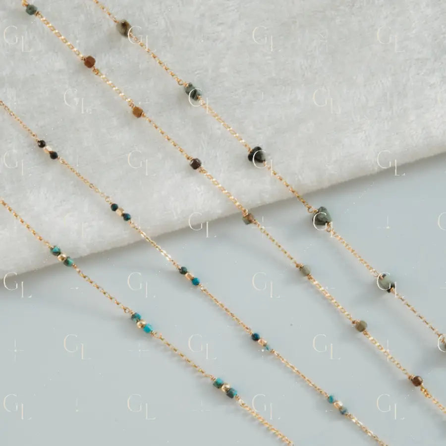 Gold chain necklace with green and brown beads on a light gray background