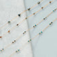 Two delicate beaded necklaces on a light blue fabric background