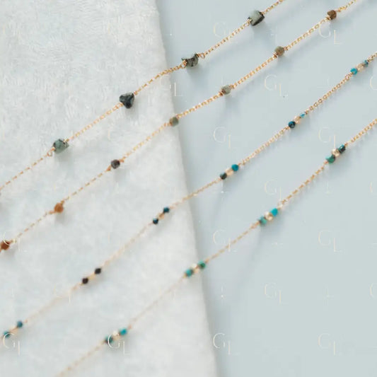 Two delicate beaded necklaces on a light blue fabric background