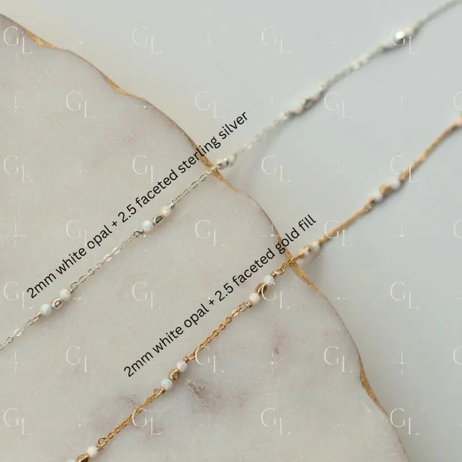 Two gold necklaces with white opal beads on a marble surface