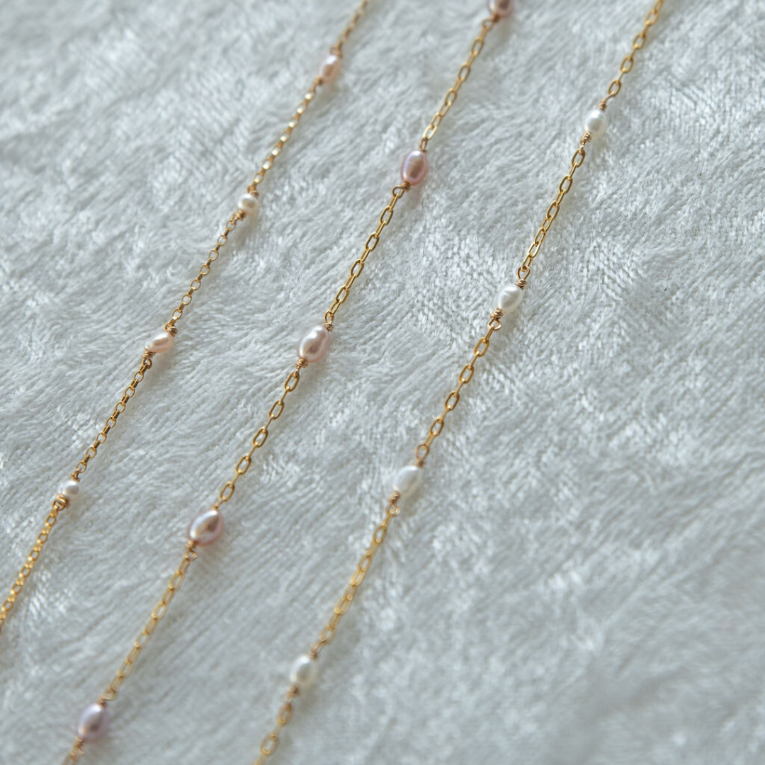 Gold chain necklace with pink pearls on a light gray background