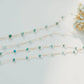 Gold chain necklace with turquoise beads on a light gray background