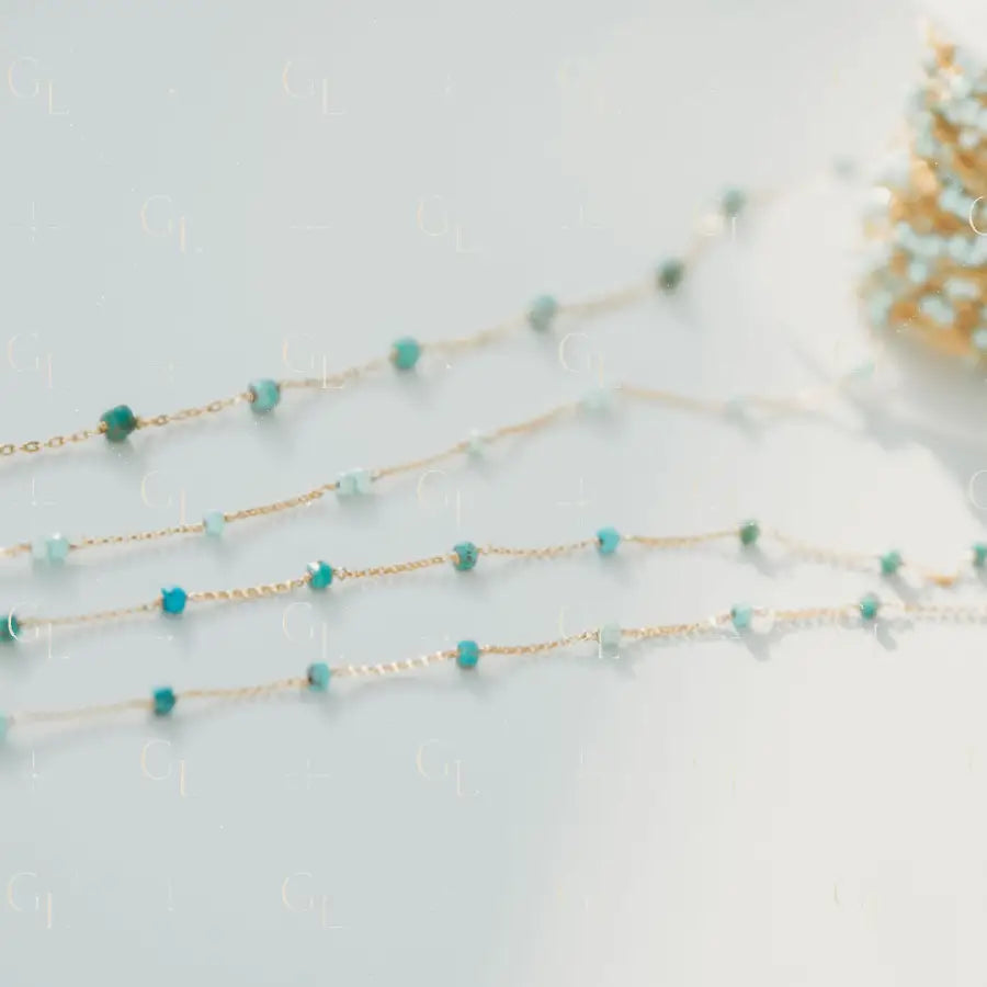 Gold chain necklace with turquoise beads on a light gray background
