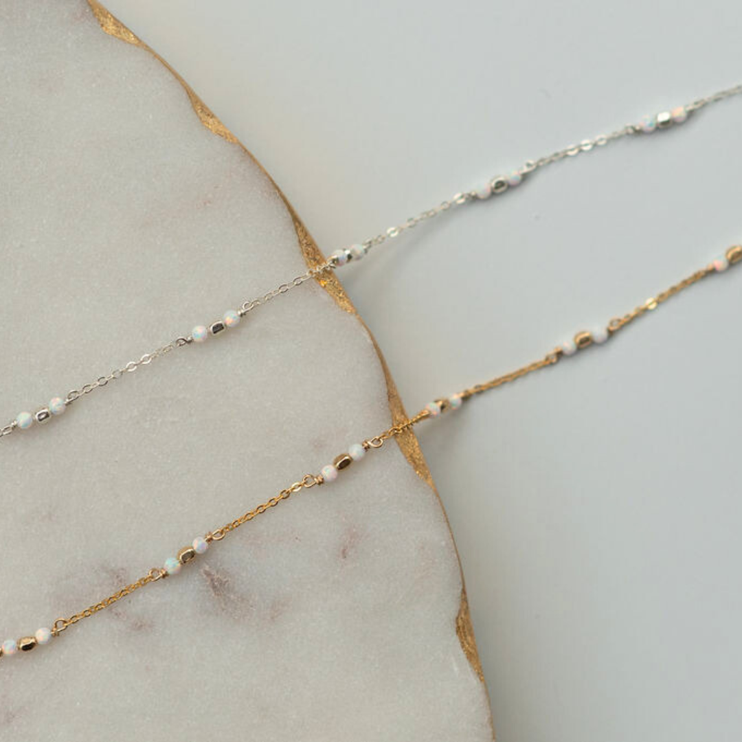 Two gold and silver beaded necklaces on a marble surface